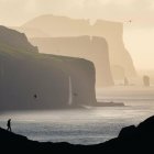 Sunset coastal scene: silhouetted figures on cliffs with crashing waves.