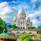 Pastel-colored church with blue dome near serene pond and lush greenery under cloudy sky