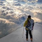 Climber in gear faces snowy mountain peaks with swirling clouds