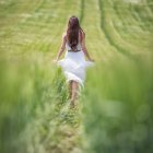 Woman in white dress walking through shallow waterway surrounded by lush greenery