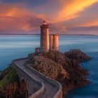 Lighthouse on rugged cliff at sunset with calm seas and colorful sky