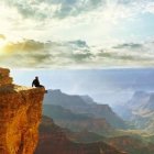 Person sitting on cliff edge admiring sunset over serene landscape