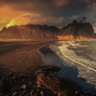 Colorful beachscape with rolling waves and mountain backdrop at sunset