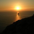 Sailing ships at sunset on calm sea with sun and waves.