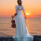 Woman in white dress playing violin at sunset by the sea