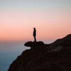 Person admiring vibrant sunset over sea from cliff