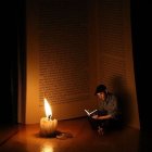 Person reading book under hanging lantern in dimly lit setting