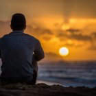 Person sitting on sand dunes watching colorful sunset with clouds