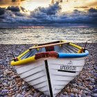 Boat on Pebbly Shore with Yacht on Horizon at Sunset