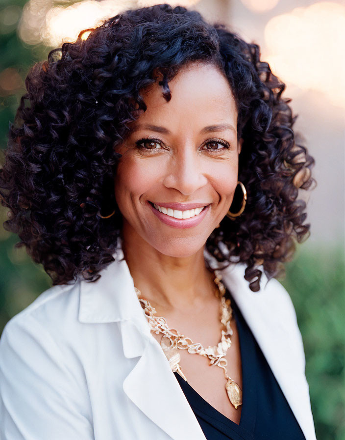 Smiling woman with curly hair in white blazer and gold jewelry