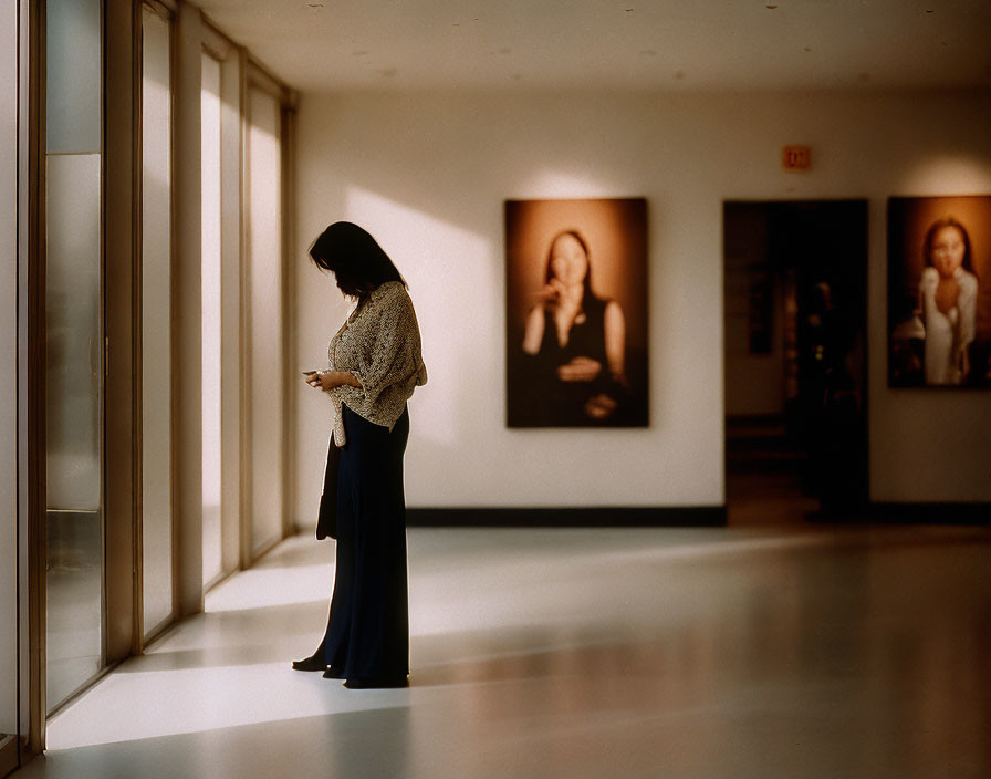 Person in Gallery Hallway with Cell Phone and Framed Portraits