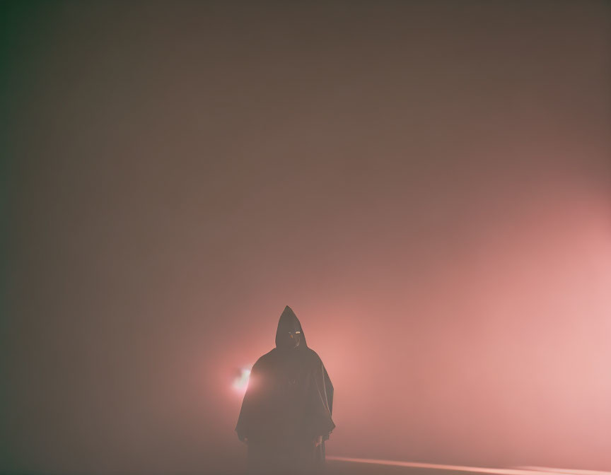 Mysterious silhouette in hooded cloak amid foggy setting