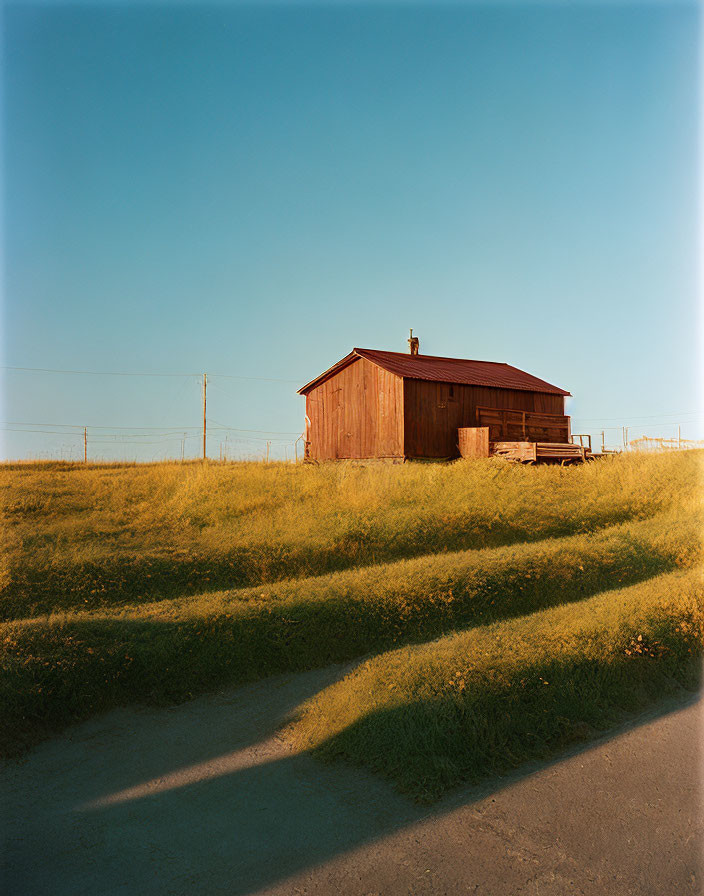 Rustic wooden barn on green hill with telephone poles against blue sky