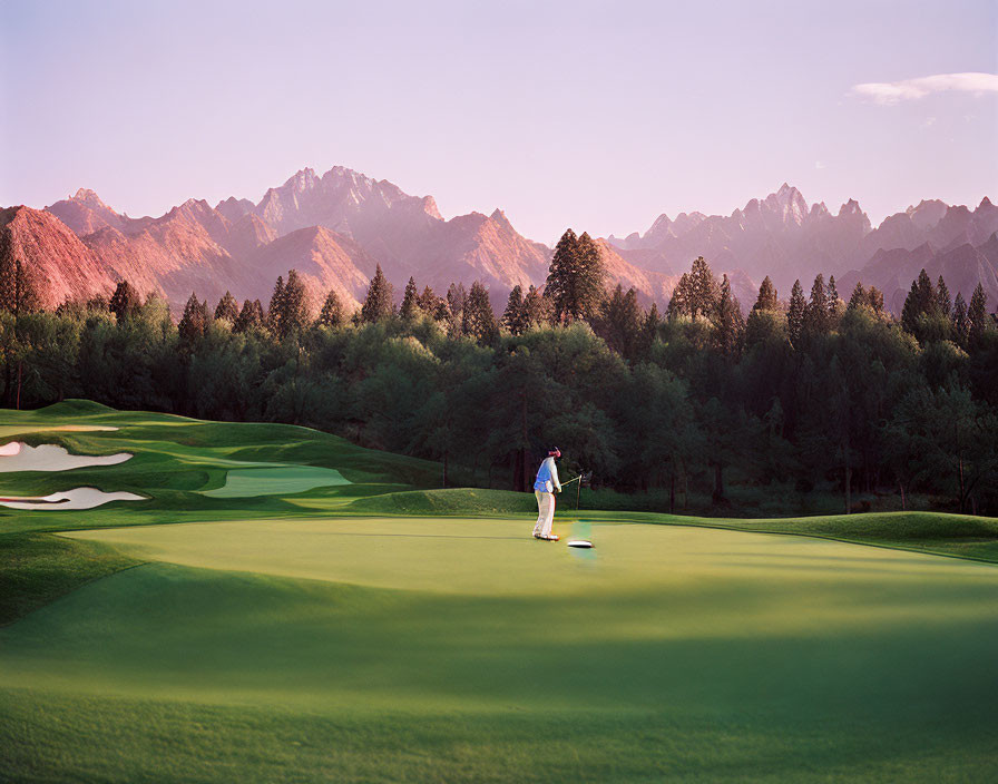 Golfer on lush green course with twilight mountains