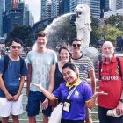 Tourists posing at iconic Merlion statues in Singapore.