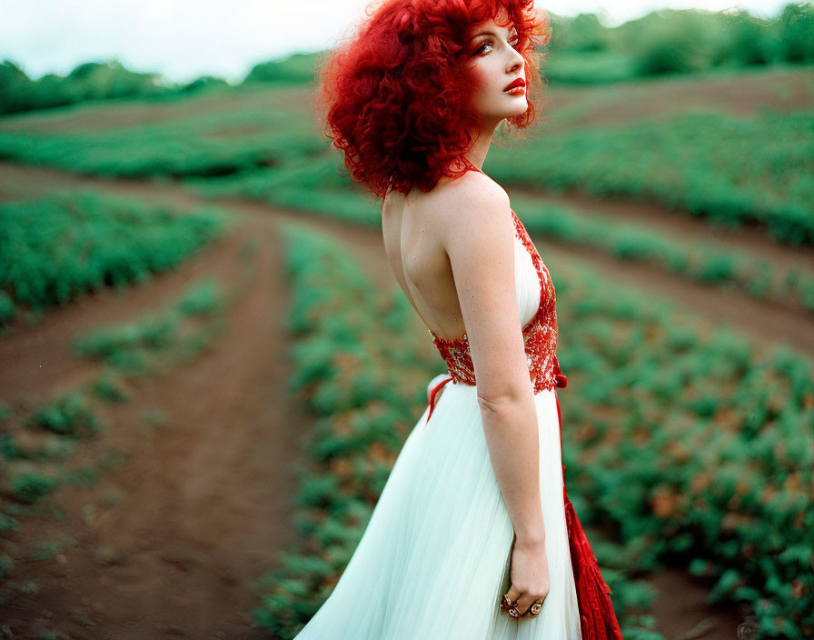 Vibrant red-haired woman in white and red dress standing in green field.