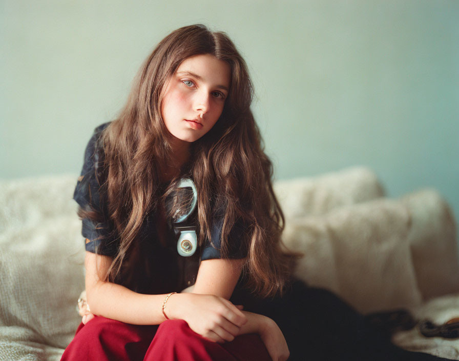 Young woman with long brown hair in contemplative pose wearing dark blouse and red bottoms.