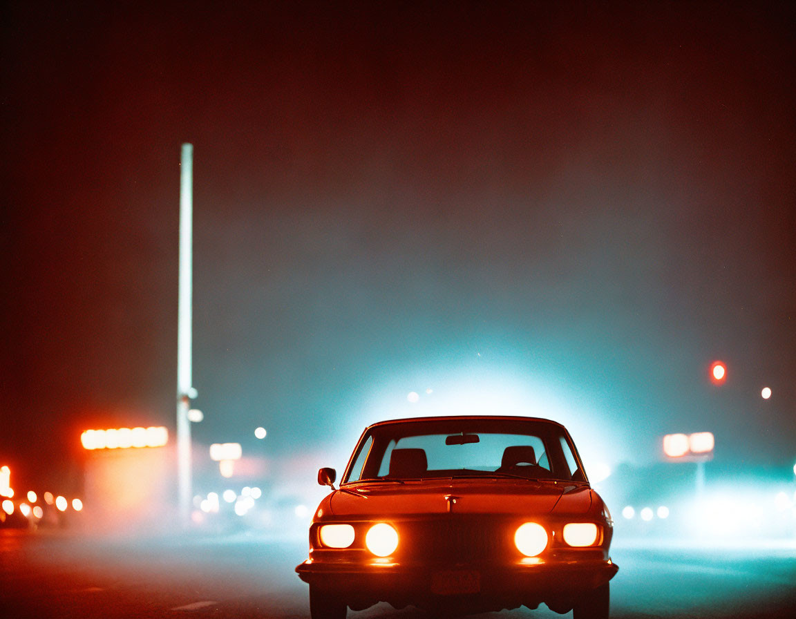 Vintage car with headlights in nighttime fog and streetlights glow