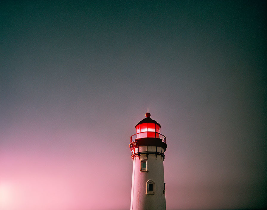 Lighthouse illuminated in twilight sky with pink and dark blue hues