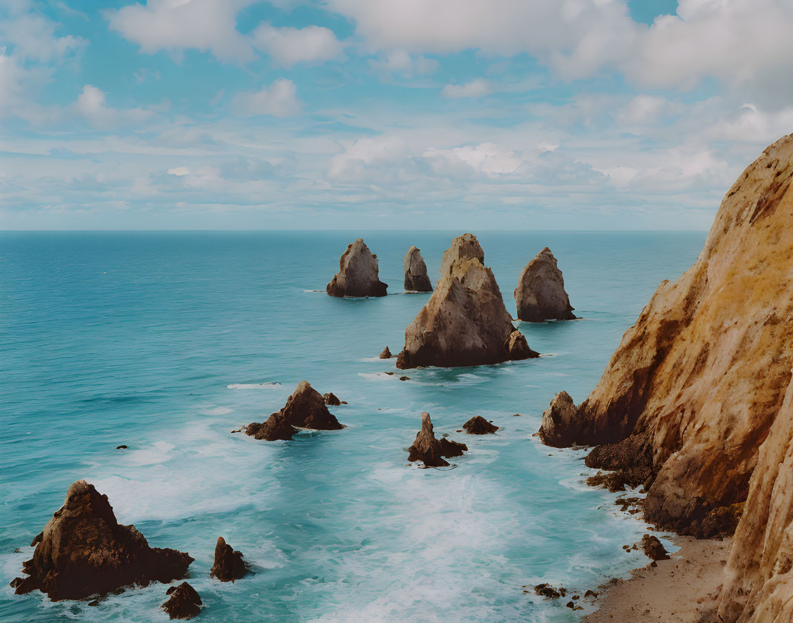 Turquoise waters with rocky sea stacks and sandy cliff under cloudy sky