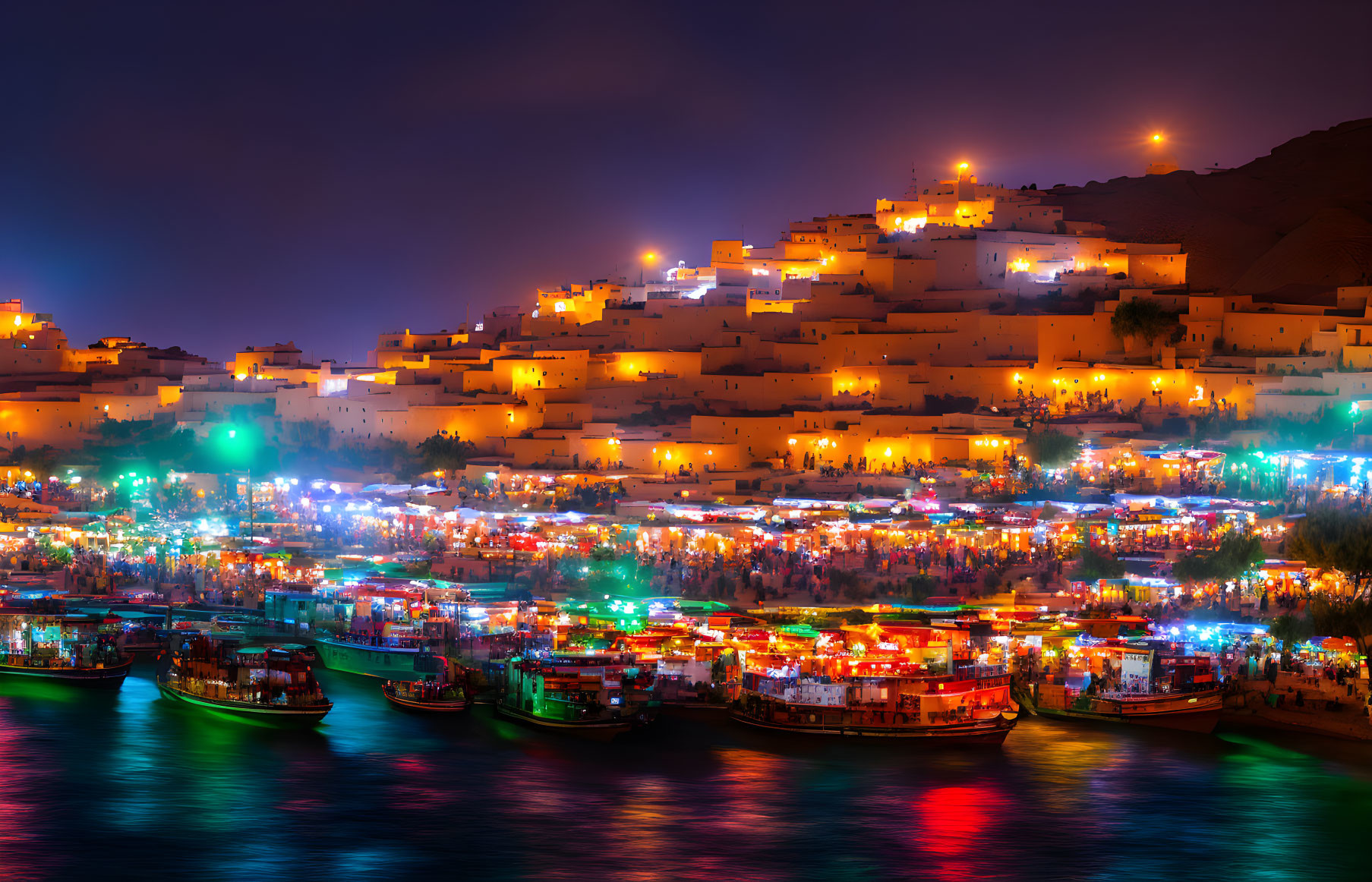 Night scene of illuminated riverside boats and glowing hillside town.