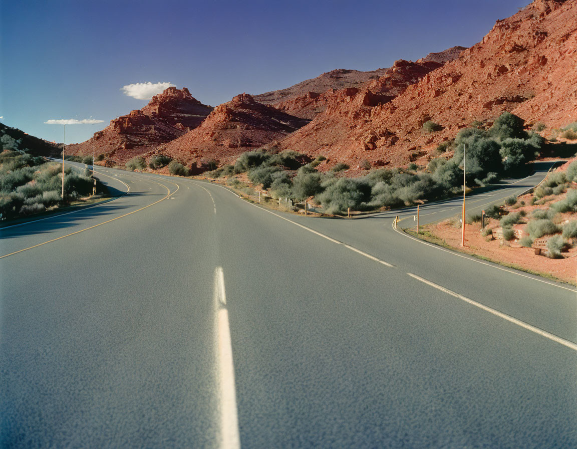 Desert road surrounded by red rocky hills and sparse greenery