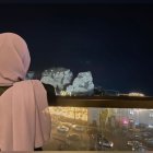 Person in pink hijab gazes at illuminated castle at night