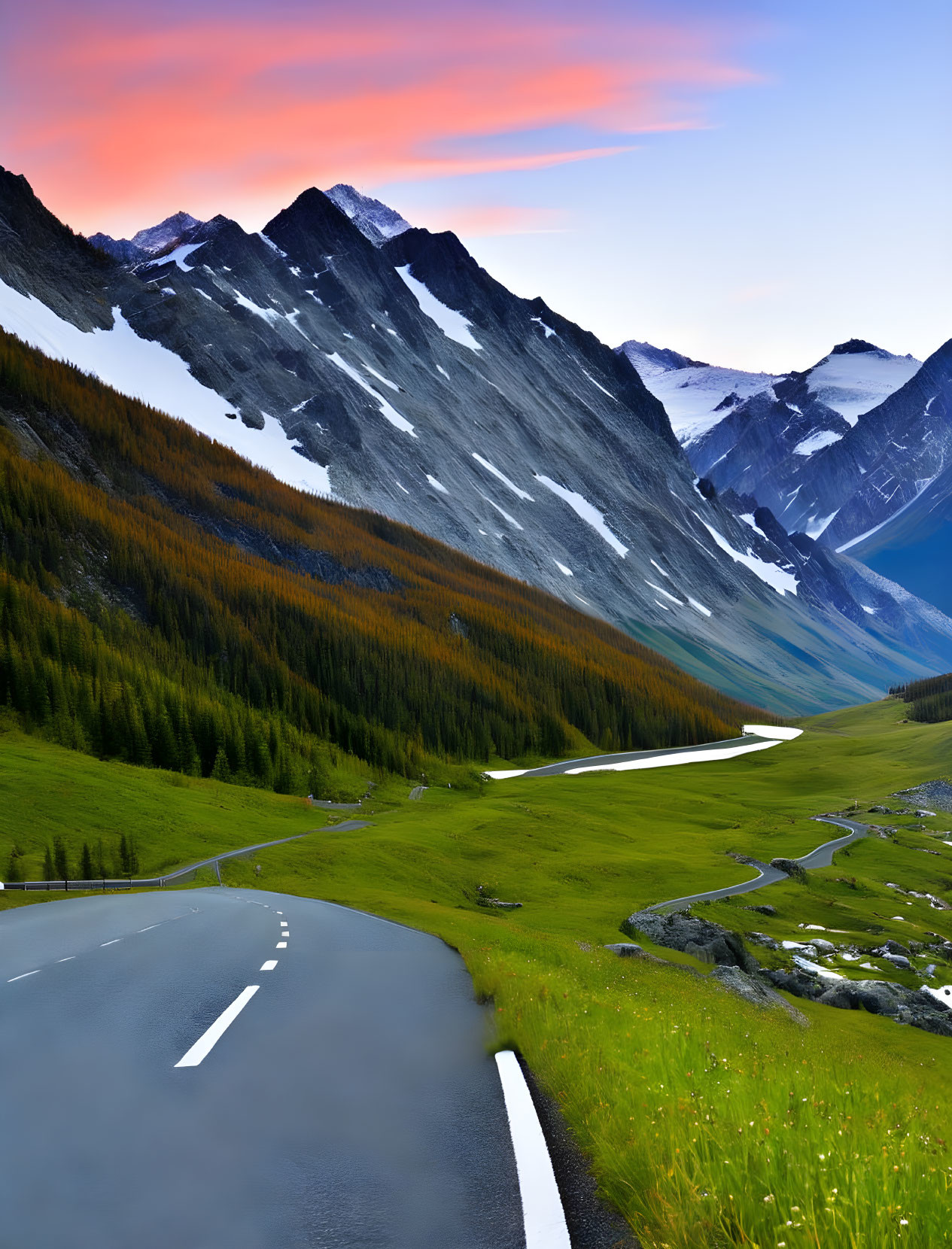 Scenic winding road through lush valley to snow-capped mountains