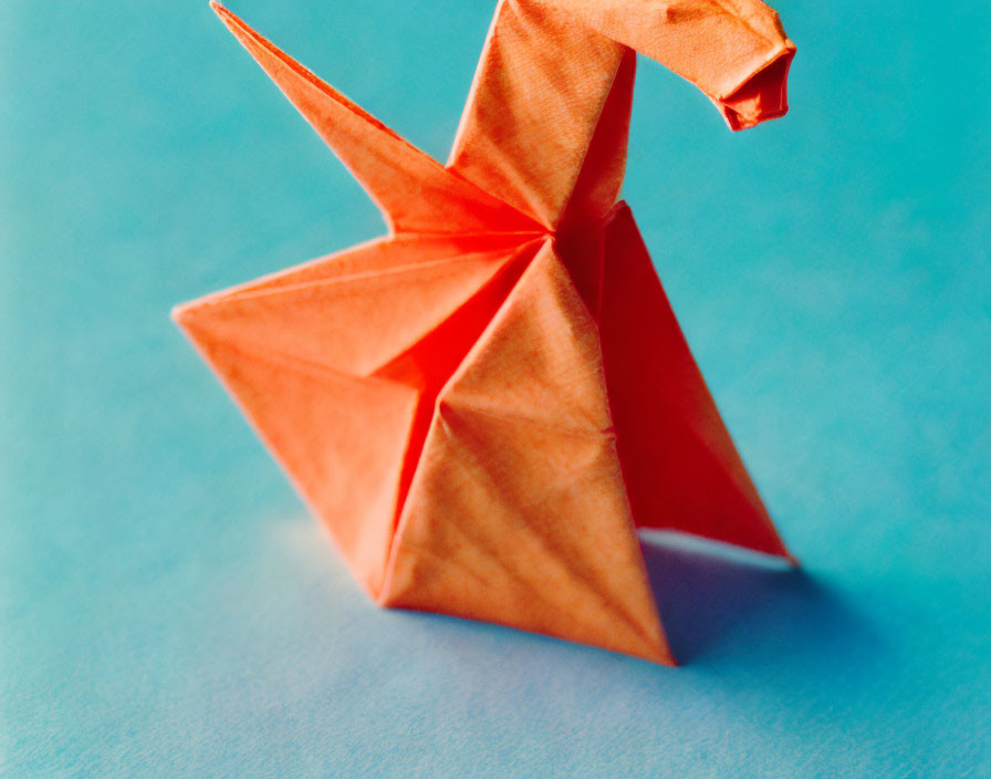 Orange Origami Crane on Blue Background: Intricate Folds and Sharp Angles