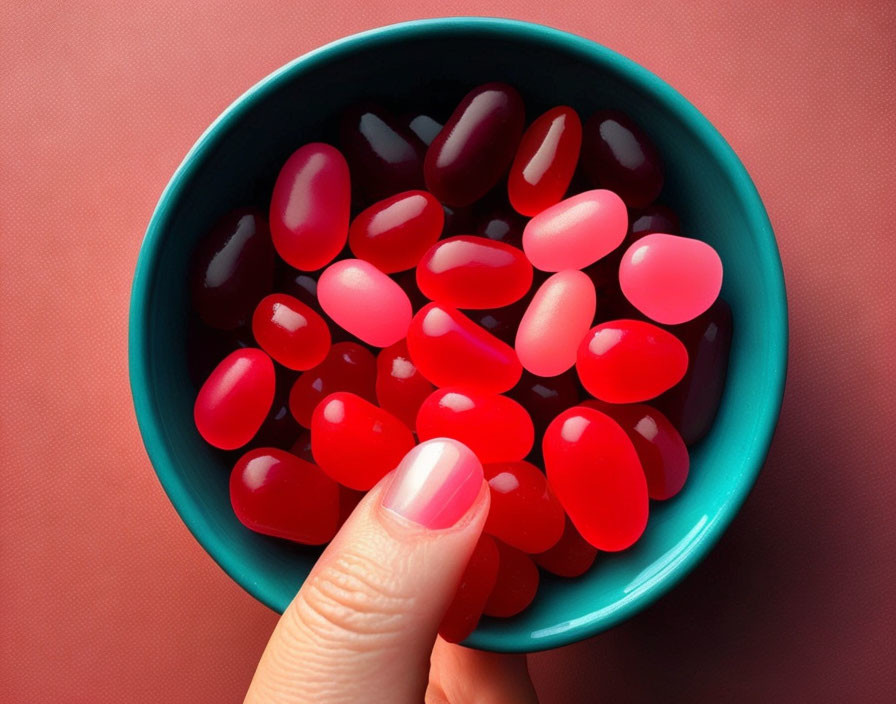 Fingers holding teal bowl with red and pink jelly beans