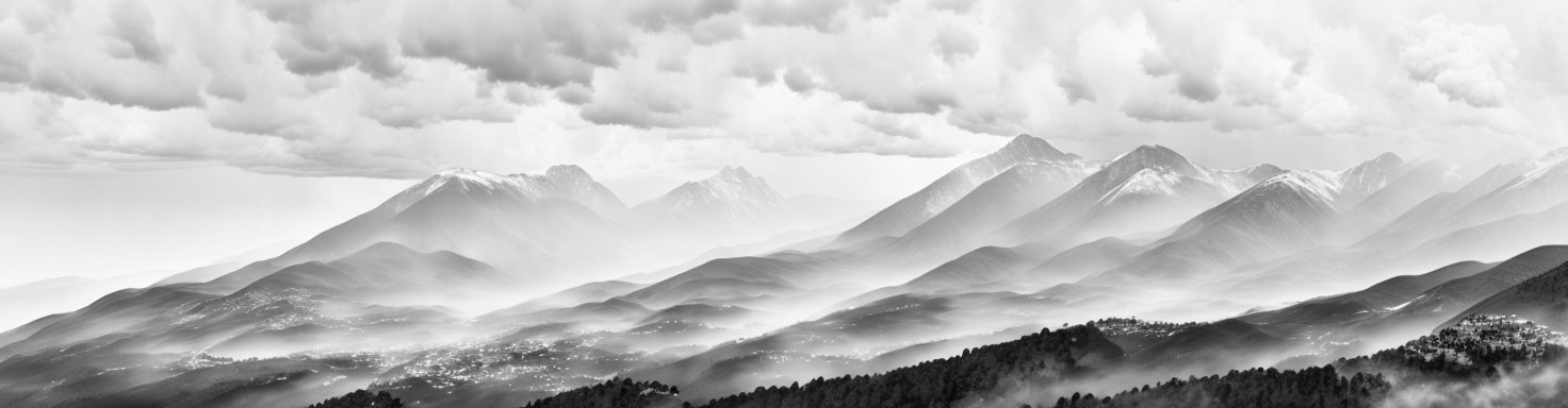 Mountain range landscape in black and white with misty valleys and sunlit peaks.