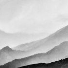 Mountain range landscape in black and white with misty valleys and sunlit peaks.