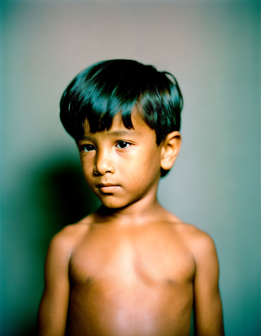 Dark-haired shirtless child stares at the camera.