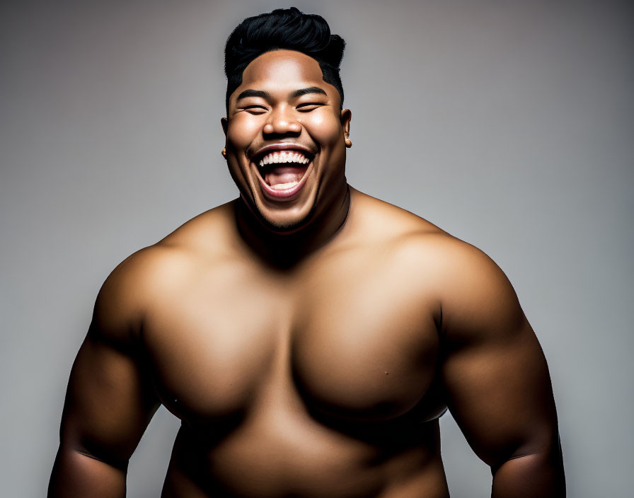 Muscular man laughing shirtless on grey background