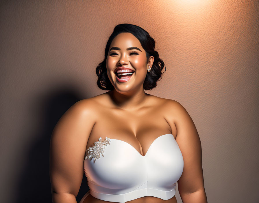 Joyful woman with dark wavy hair in white top against warm backdrop