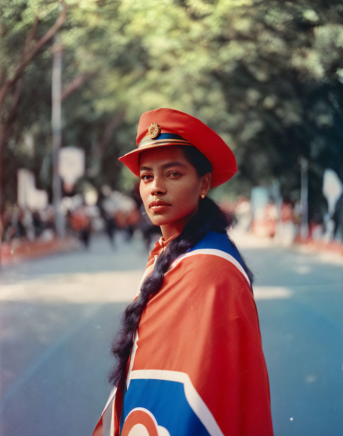 Confident young woman in red hat and sash, surrounded by blurred crowd and trees