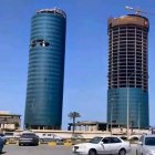 Twin blue glass cylindrical towers in urban setting with cars