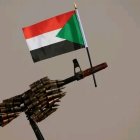 Sudanese flag draped over AK-47 rifle against clear sky