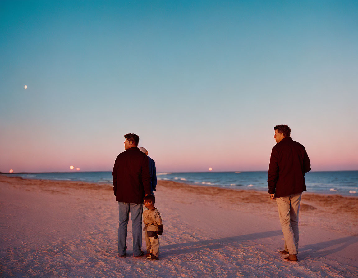 Men and child on beach at twilight with serene sea and moon in clear sky