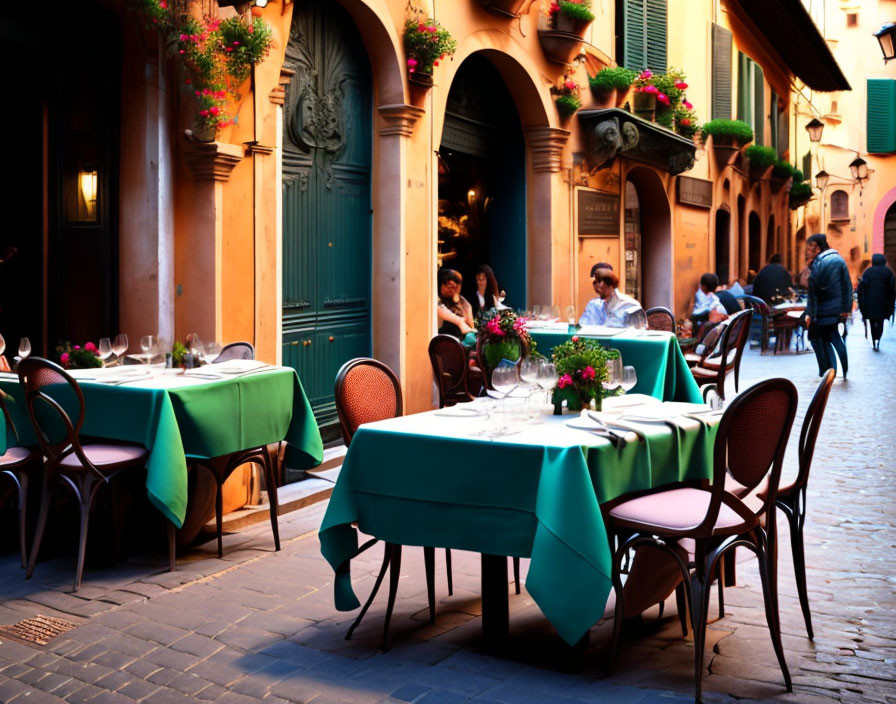 Empty outdoor dining setup on quaint street with green tablecloths.