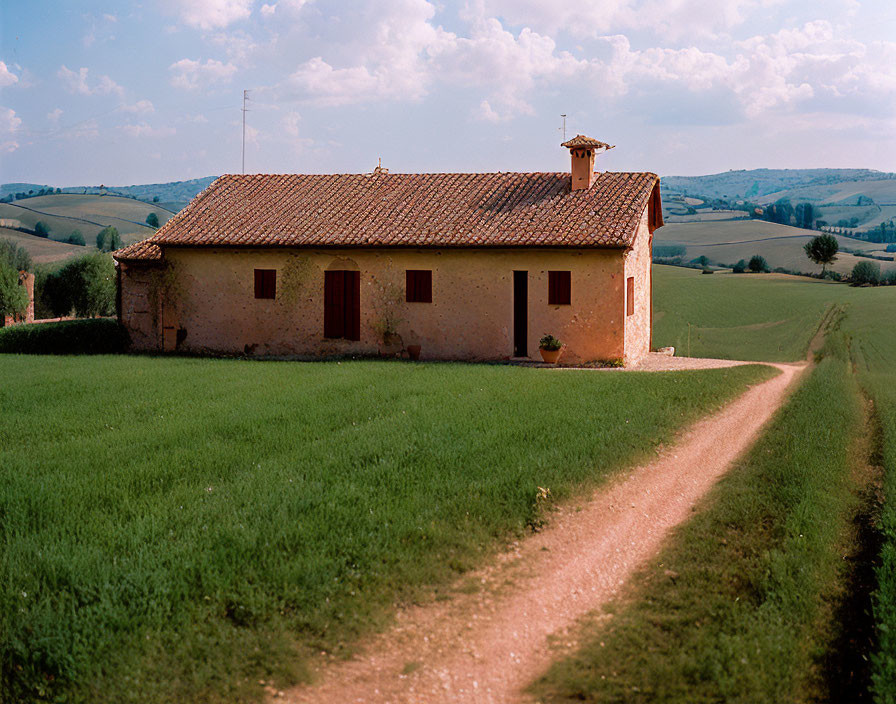 Rustic house with red-tiled roof in green hills under clear sky