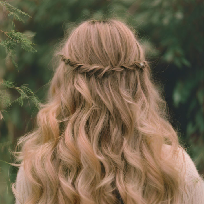 Blond person with braided crown, greenery backdrop