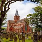 Medieval church with spire, surrounded by lush trees and figures in period clothing