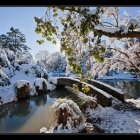 Winter village scene: snow-covered houses, river, bridge, falling snow, twilight sky