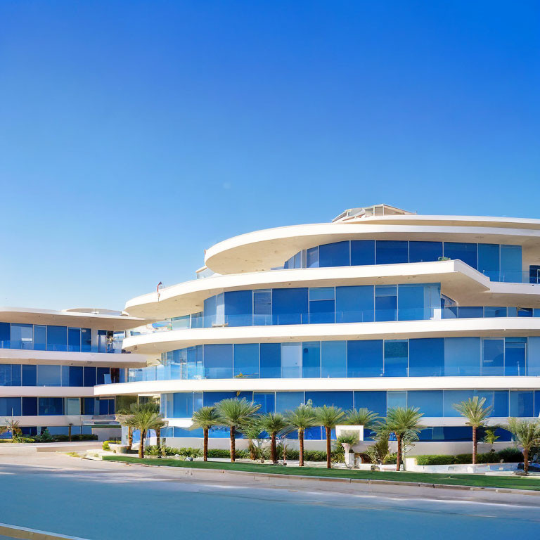 Curved modern building with blue glass windows and palm trees on street.