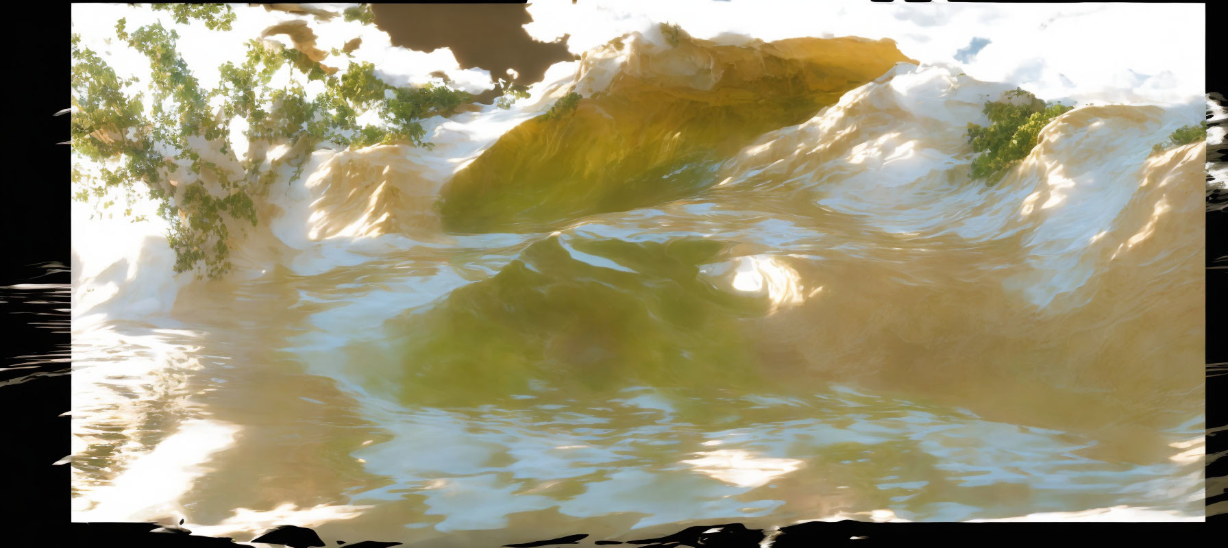 Sunlit golden cliffs with lush green foliage reflected in rippling water