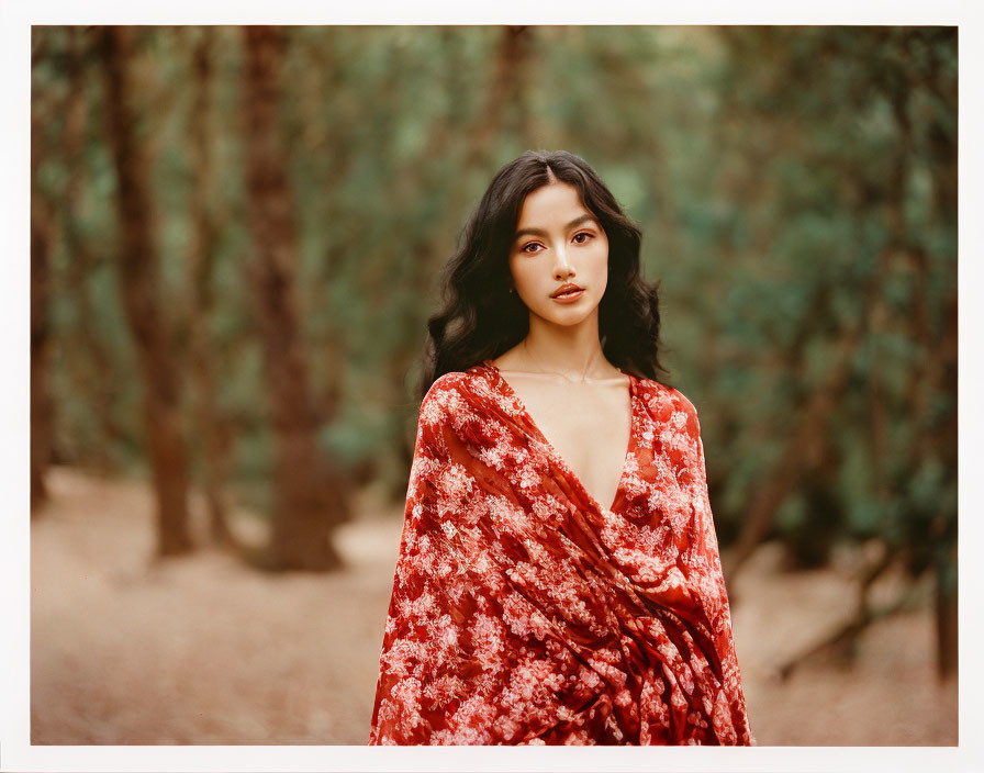 Woman in red floral garment posing in front of forest backdrop