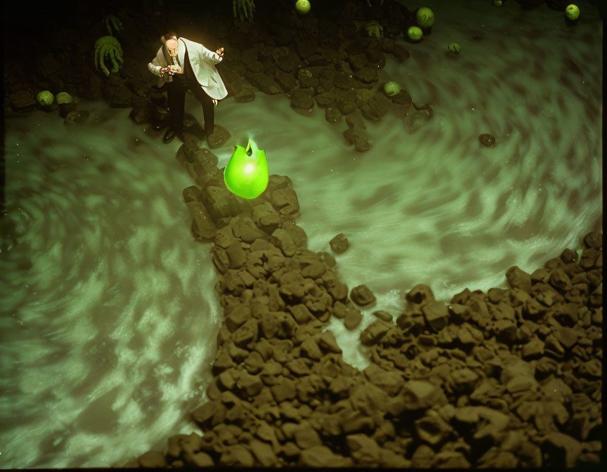 Person in suit near glowing green orb and swirling water vortex surrounded by rocks.