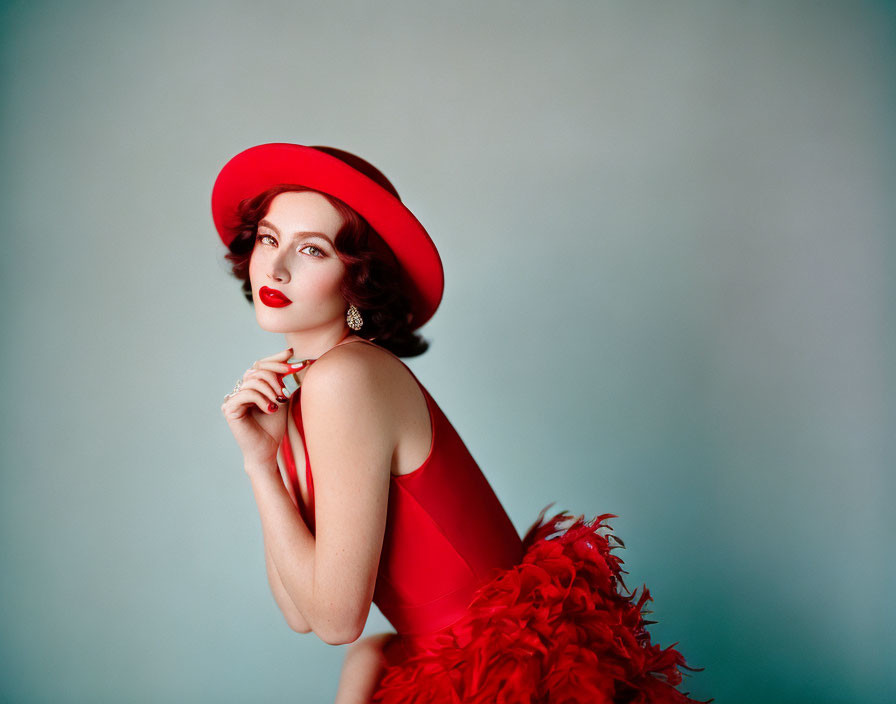 Woman in Red Hat and Dress Poses Against Teal Background