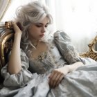 Elegant woman with wavy hair in grey gown by sunlit window